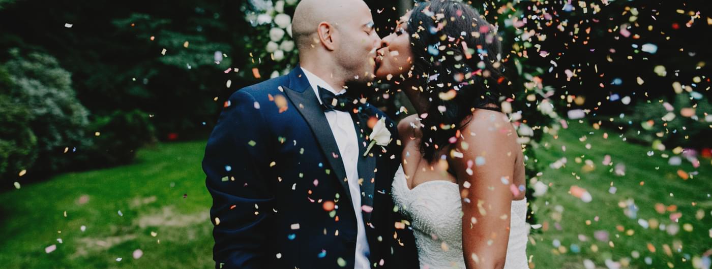 Couple in wedding attire kissing underneath confetti